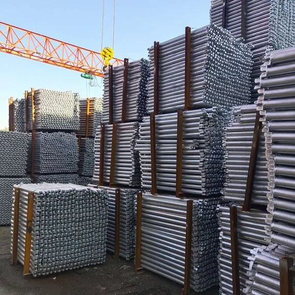 Stacked bundles of galvanized scaffolding tubes under a gantry crane
